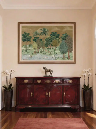 Framed Ranthambore Forest wall art in forest green above a carved mahogany sideboard with a bronze horse and white orchids in a formal hallway.