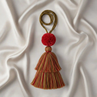 Flat lay photo of the Autumn Flame Tassel on a white silk background, highlighting the vibrant red pom-pom and two-tier tassel design.