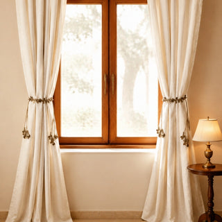 Regal Gilt antique gold beaded tiebacks cinching ivory linen curtains beside a wooden side table