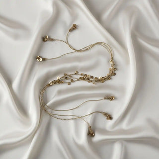 Flat lay of the Regal Gilt Tassel showing the thin gold chains and the cascade of metallic sequins/leaves on a satin background.