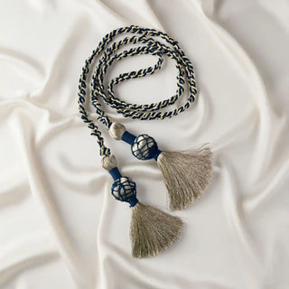 Flat lay of the Regal Twist Tieback showing the braided gold and navy cord and the two caged tassel ends on a white silk background.