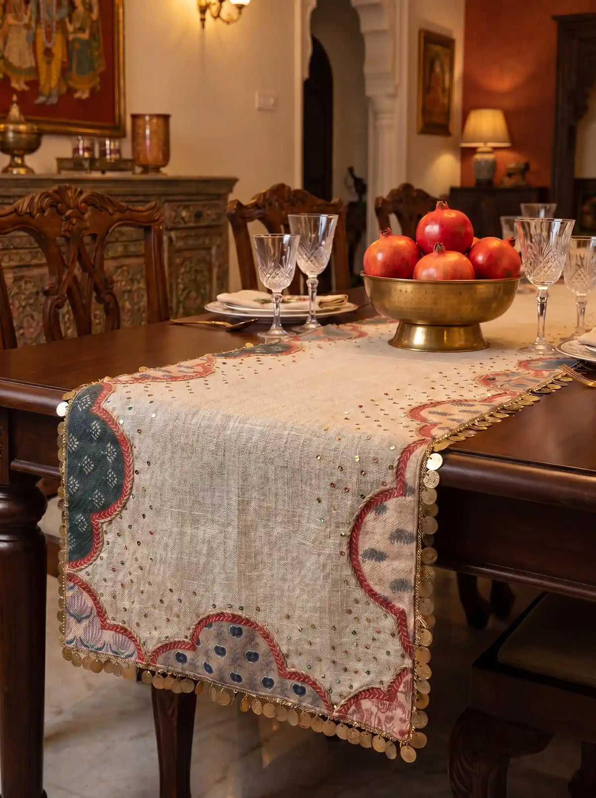 Block-printed linen runner with gold coin trim under a brass bowl of pomegranates