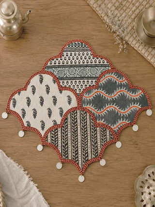 A symmetric flatlay product shot of the cloud-shaped Riwaayat patchwork linen table mat showing all four block-printed Mughal patterns.