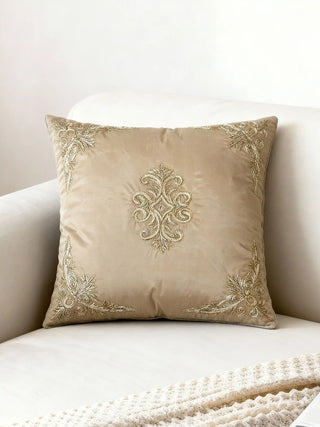 Rocaille Charm cushion cover in champagne satin displayed on a cream velvet armchair with gold corner embroidery.