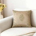 The Rocaille Charm gold embroidered silk cushion cover styled elegantly on a plush off-white sofa panel next to yellow flowers.
