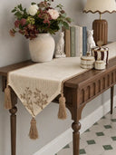 The Rooted Grace Table Runner in Ivory & Taupe on a wooden console table, styled with a stone vase, ceramic cats and books.