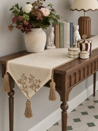 The Rooted Grace Table Runner in Ivory & Taupe on a wooden console table, styled with a stone vase, ceramic cats and books.