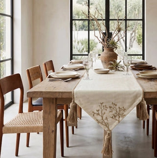 The Rooted Grace table runner styled down the center of an organic wooden dining table paired with woven cane back chairs.
