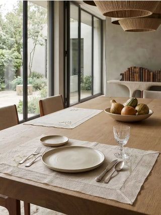 A pair of Rooted Grace open-weave cream linen table mats styled with matte ceramic plates on an organic rustic wood dining table.