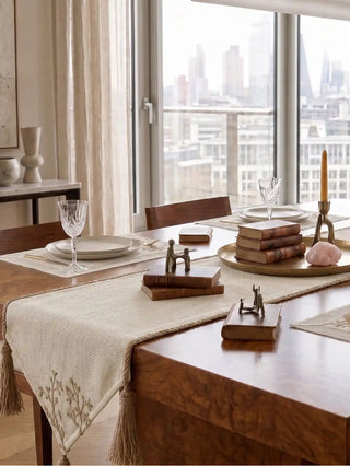 The Rooted Grace table runner and matching Eden placemats styled across a luxury wooden tablescape with a modern city view background.