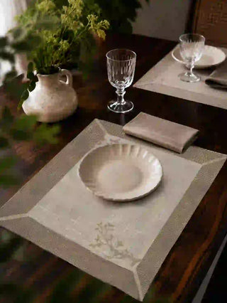 Rooted Grace table mats in cream linen with sage botanical borders styled in a formal dining setting with white plates, crystal glassware, and fresh greenery.