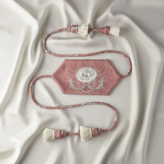 Flat lay of the Rosette Royale Tassel showing the hexagonal rose velvet panel with crest embroidery and four white fringe tassels.