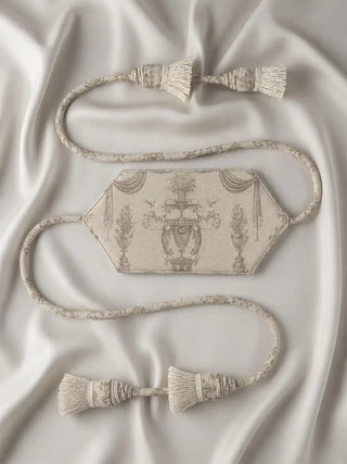 A high-resolution flatlay product shot of the Rosette Royale cream curtain tieback displaying its hexagonal embrace band and trailing tassels on satin.