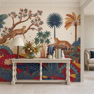 Royal Jungle Safari wallpaper behind a cream carved console table with a pleated-shade lamp, a glass vase of orange and white flowers and two white cat figurines beside books.
