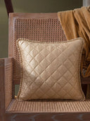 The Rukhsar quilted gold silk cushion cover with a ruffled edge styled beautifully on a modern wooden cane-back armchair.