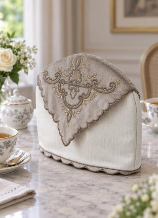 The Rumi tea cosy in Cream, view-diningtable beside patterned teacups and a sugar bowl.