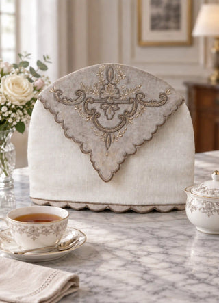 The Rumi tea cosy in Cream, view-marbletable beside white roses and a teapot.
