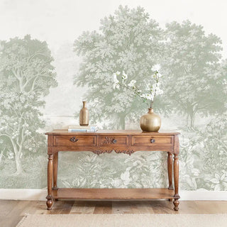 The Saanjh sage green forest mural styled behind a vintage wooden sideboard with a gold vase in a luxury living room.