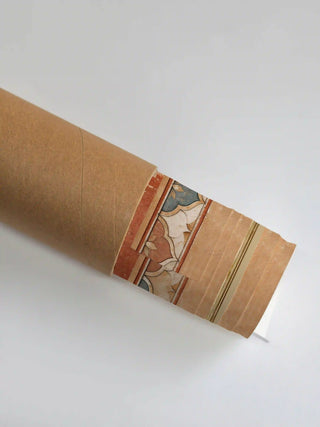 The rolled edge of the Sacred Stillness wall art peeking out of a brown kraft tube, showing the terracotta and slate scalloped border.