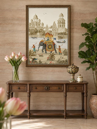 The Safar embroidered wall art in a dark wood frame above a carved walnut console with pink tulips, a lidded urn and a tall leafy plant.
