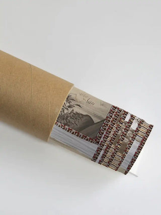 The Safar wall art partially unrolled from its kraft paper shipping tube, showing a beaded border and a river scene in muted tones.