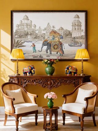 Safar Embroidery wall art displayed in a rich mustard living room above a hand-carved console with rattan chairs.