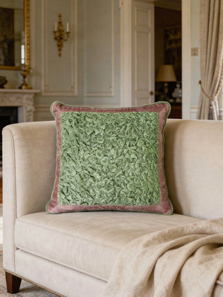 A luxury spring-green crushed velvet cushion with a rose-pink border styled on a cream sofa in a classical room.