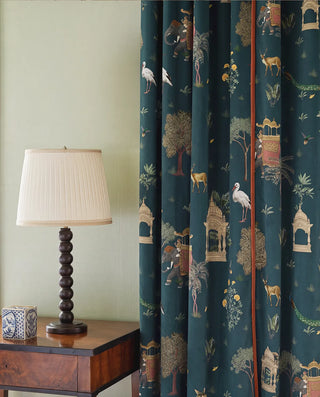 Floor-to-ceiling drapes in Sair Blue teal velvet with terracotta piping next to a classical table lamp.