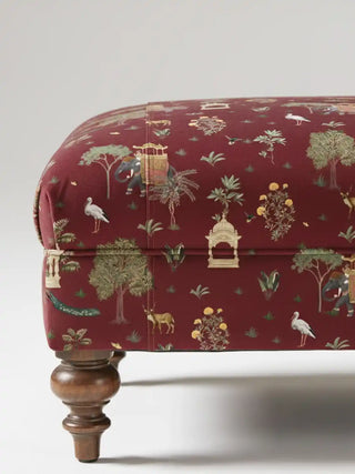 Close up of a luxury ottoman upholstered in Sair Red fabric, highlighting the rich crimson textile and intricate wildlife motifs.