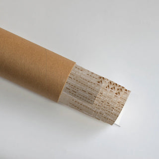 The Secret Garden embroidered wall art partially unrolled from its kraft paper shipping tube, showing the willow tree design in Blush & Bronze.
