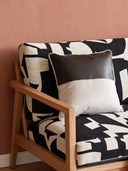 A luxury Serene Strokes Fusion cushion featuring a chocolate leather panel and cream velvet resting on a black and white patterned armchair.