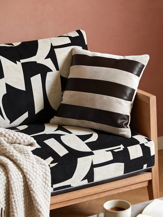 A luxury Serene Strokes stripe cushion with bold charcoal and cream bands resting on a graphic patterned armchair.