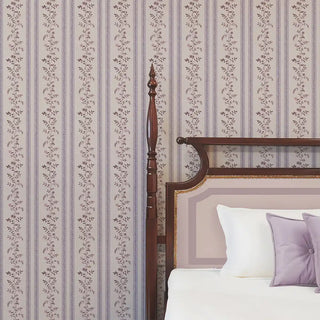 Lavender & beige floral stripe wallpaper behind a wooden bed with lilac cushions, creating a soft coordinated look.