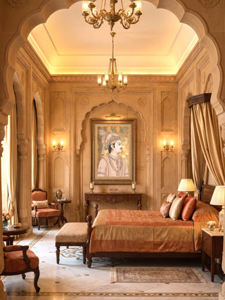 Shahenshah-e-Riyasat wall art in a gilt frame above a carved wooden console in a sandstone-arched bedroom with a brass chandelier and copper silk bedding