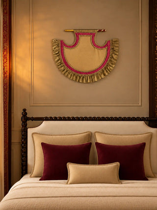 Shahi Bijna decorative fan on a panelled beige wall above a cream bed with maroon cushions, hung from a gold and red rod.