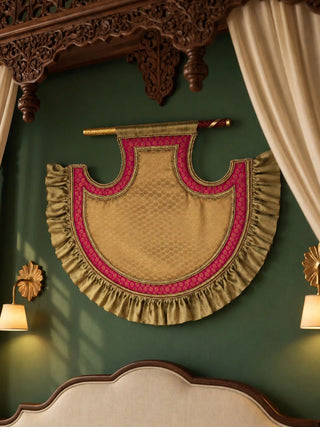 The Shahi Bijna fan on a green wall: a golden jacquard body with a rani pink brocade border, gold piping and a pleated ruffle edge.