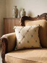 The Shahzar embroidered linen cushion cover styled elegantly on a classical carved wooden armchair panel in a warmly lit room.