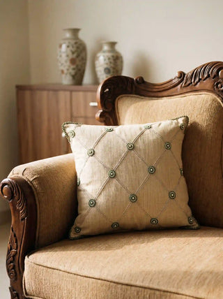 The Shahzar embroidered linen cushion cover styled elegantly on a classical carved wooden armchair panel in a warmly lit room.