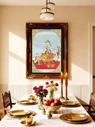 A framed Shiv Parivar mural displayed on a cream wall above a white dining table set with gold accents.