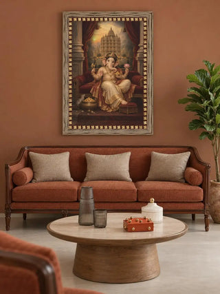 Shree Vinayaka Darbar portrait wall art in a silver-grey carved frame hanging above a rust sofa with grey cushions, beside a round wooden coffee table