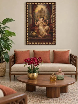Shree Vinayaka Darbar framed wall art displayed above a cream sofa with rust cushions, beside a wooden coffee table, potted green plant and decorative accessories.