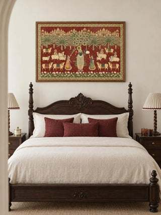 The Shrinathji Madhuban wall art in Maroon & Gold, framed and hung above a dark wood carved bed with cream linens and burgundy cushions.