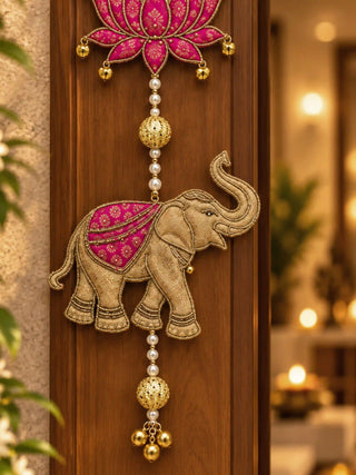 Close-up of a Shubh hanging: a gold brocade elephant with a magenta saddle cloth below a lotus, on pearl strings with gold bells.