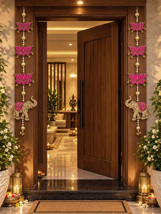 Shubh hangings on a wooden door frame with lanterns and flowers below, magenta lotuses, gold beads and elephants facing inward.
