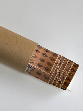 The Shyam Sundar embroidered wall art partially unrolled from its kraft paper shipping tube, showing the ochre diamond-pattern border.