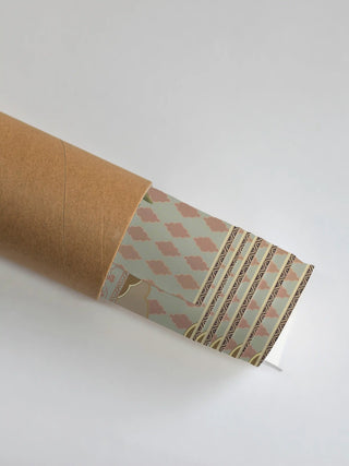 The Shyam Sundar wall art rolled in a kraft cardboard tube, with the coral and sage patterned border showing at the open end.