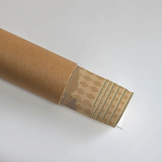 The Shyam Sundar wall art rolled in a kraft cardboard tube, with the beige cloud-lattice and geometric border showing at the open end.