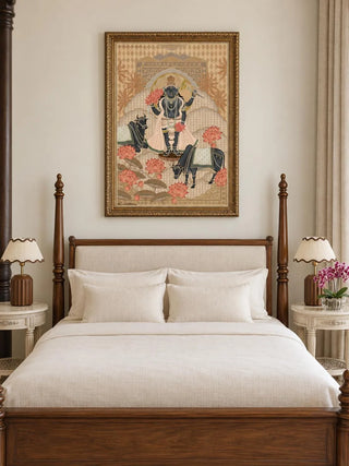 The Shyam Sundar wall art in Beige & Coral, in an ornate gold frame, above a four-poster wooden bed with cream linen and two scallop-shade bedside lamps.