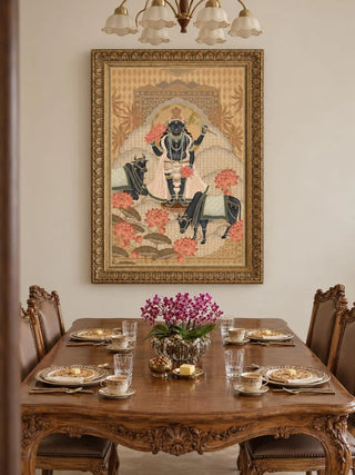 The Shyam Sundar wall art in Beige & Coral, in an ornate carved gold frame, on a cream dining room wall above a carved wooden table set with plates, teacups and magenta orchids.