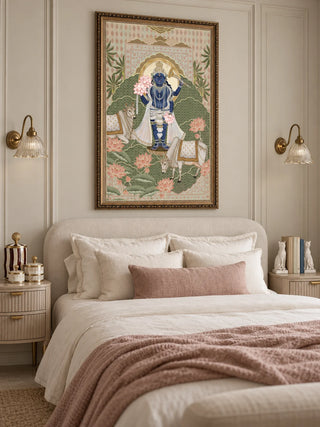 The Shyam Sundar wall art in Sage & Coral, in an ornate gold frame, above a cream upholstered bed between two brass wall lamps.